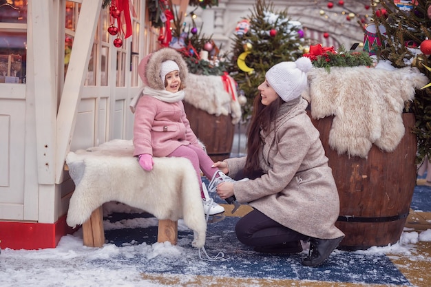 Esporte de inverno em família no parque A mãe ajuda sua filha a colocar patins Fundo de Natal Conceito de férias de natal e inverno em família