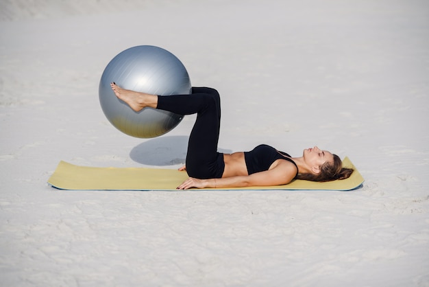 Esporte e conceito de estilo de vida saudável. Menina bonita fitness fazendo exercícios de estômago com ajuste bola na praia. Jovem mulher fazendo exercícios de pilates.