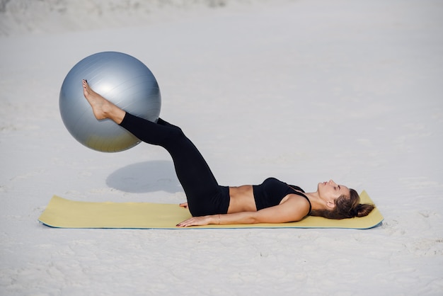 Esporte e conceito de estilo de vida saudável. Menina bonita fitness fazendo exercícios de estômago com ajuste bola na praia. Jovem mulher fazendo exercícios de pilates.