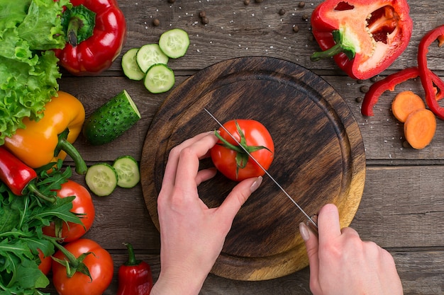 Esporte e dieta. Vegetais Em Fatias. Pimentas, tomates, salada em fundo rústico. Vista do topo. Copie o espaço. Mãos que cortam um tomate em uma tábua