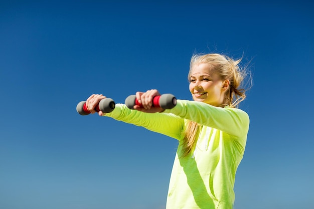 Esporte e estilo de vida - jovem mulher desportiva com halteres leves ao ar livre