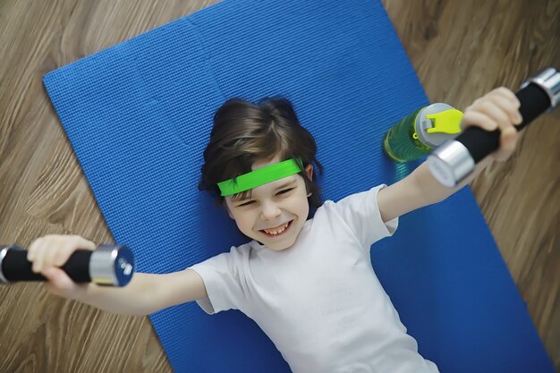 Esporte e estilo de vida saudável. Criança praticando esportes em casa. Haltere de tapete de ioga e corda de pular. Currículo desportivo com conceito de exercícios em casa.