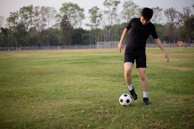 Esporte e recreação conceito um jogador de futebol vestindo camiseta preta e calças praticando chutando a bola no campo gramado.