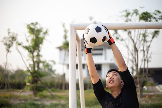 Esporte e recreação conceito um jovem goleiro do sexo masculino usando as duas mãos para pegar a bola para evitar que o time adversário marque.