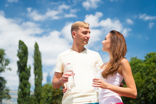 Esporte e saúde. Mulher e homem bebem água da garrafa. Atividade e energia de verão. Menina e cara ensolarado ao ar livre. O casal do treinador relaxa após o treino.