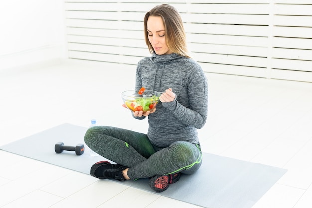 Esporte, estilo de vida saudável e conceito de pessoas - jovem mulher com salada e um haltere sentado no