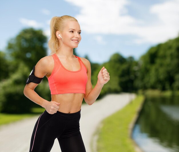 esporte, exercício, tecnologia, internet e saúde - mulher desportiva sorridente correndo e ouvindo música do smartphone