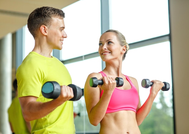 esporte, fitness, estilo de vida e conceito de pessoas - sorrindo homem e mulher com halteres exercitando no ginásio
