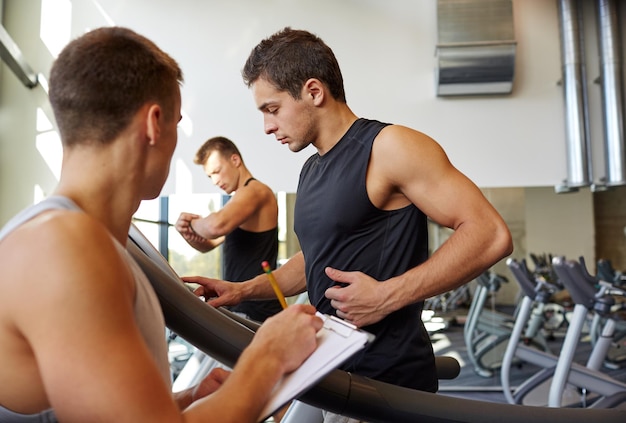 Esporte, fitness, estilo de vida, tecnologia e conceito de pessoas - homens com personal trainer exercitando em esteira no ginásio