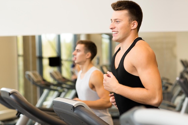 Esporte, fitness, estilo de vida, tecnologia e conceito de pessoas - homens sorridentes se exercitando na esteira no ginásio