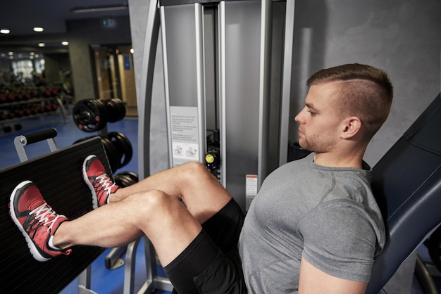 Foto esporte, fitness, musculação, estilo de vida e conceito de pessoas - homem exercitando e flexionando os músculos das pernas na máquina de ginástica