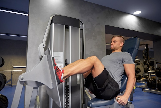 esporte, fitness, musculação, estilo de vida e conceito de pessoas - homem exercitando e flexionando os músculos das pernas na máquina de ginástica