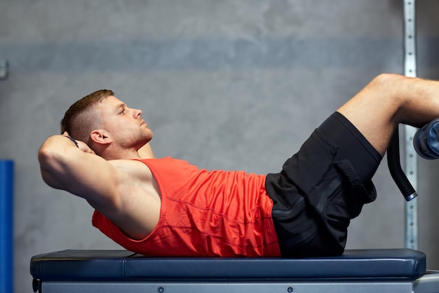 Foto esporte, fitness, musculação, estilo de vida e conceito de pessoas - jovem fazendo exercícios abdominais no ginásio