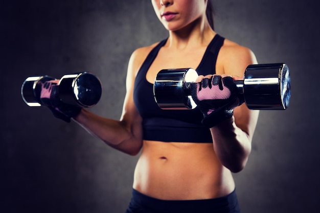 esporte, fitness, musculação, levantamento de peso e conceito de pessoas - close-up de mulher flexionando os braços com halteres no ginásio