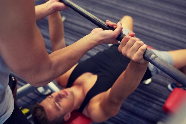 esporte, fitness, trabalho em equipe, levantamento de peso e conceito de pessoas - jovem e personal trainer com barbell flexionando os músculos no ginásio