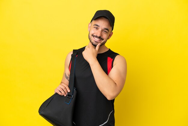 Esporte jovem homem caucasiano com bolsa esportiva isolada em um fundo amarelo feliz e sorridente.