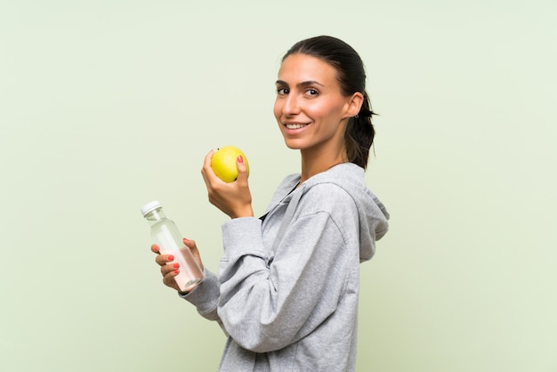 Esporte jovem mulher com uma maçã e uma garrafa de parede verde isolado de waterover