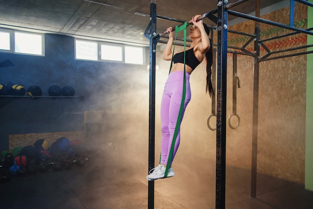 Esporte jovem mulher fazendo puxar para cima no ginásio.