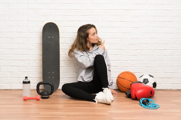 Esporte jovem mulher sentada no chão apontando para trás com o dedo indicador