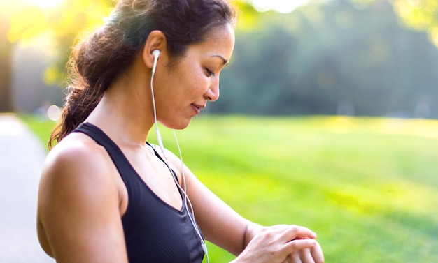 Esporte mulher asiática ouvir música com fones de ouvido enquanto olha para o relógio ao ar livre