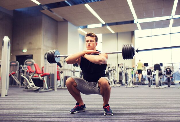 esporte, musculação, estilo de vida e conceito de pessoas - jovem com barra fazendo agachamentos no ginásio