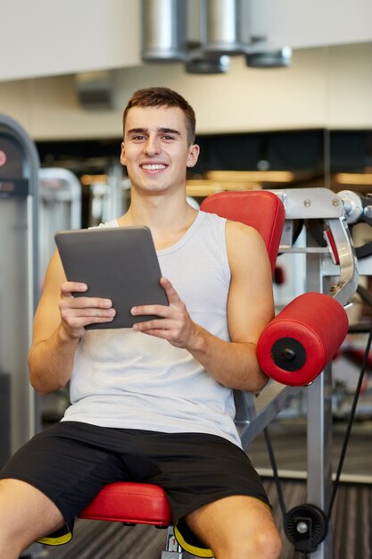 esporte, musculação, estilo de vida, tecnologia e conceito de pessoas - jovem sorridente com computador tablet pc no ginásio