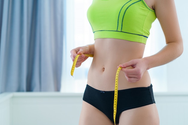 Esporte saudável fitness mulher magro medindo sua cintura fina com uma fita métrica para mostrar resultados de dieta e perda de peso. Motivação e progresso no emagrecimento, atingindo metas de perda de peso