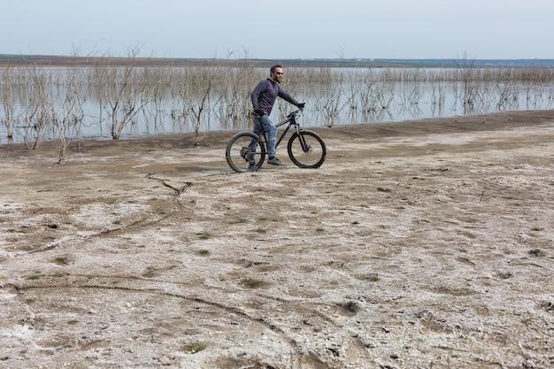 Esportes brutal barbudo em uma mountain bike moderna um ciclista em um lugar deserto de sal à beira do lago