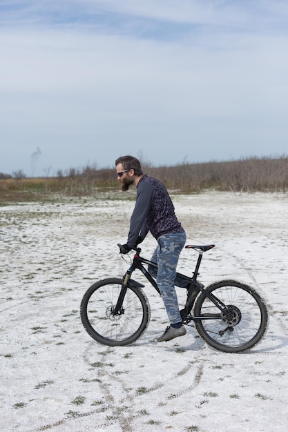 Esportes brutal barbudo em uma mountain bike moderna Um ciclista em um lugar deserto de sal à beira do lago