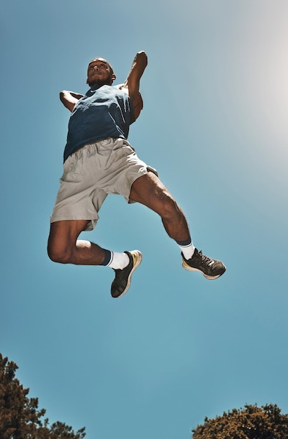 Esportes céu azul e homem de basquete saltam para competição de jogo ou prática de treinamento de slam dunk ou treino motivação de atleta de alta energia e jogador de basquete fazendo fitness ou exercício vista inferior
