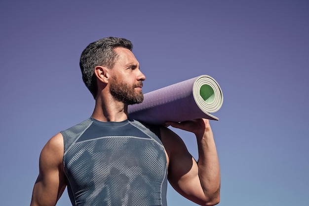 Esportes e rotina de estilo de vida saudável atleta masculino faz exercício matinal treino de ioga esportista com tapete de ioga cuidados de saúde ao ar livre cara musculoso faz esporte homem em roupas esportivas