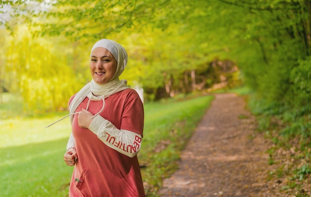 Esportes muçulmanos felizes se encaixam em mulher na trilha hijab correndo ao ar livre no parque de verão