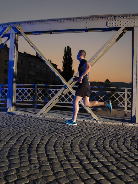 esportes urbanos, jovem saudável correndo pela ponte da cidade no início da manhã à noite