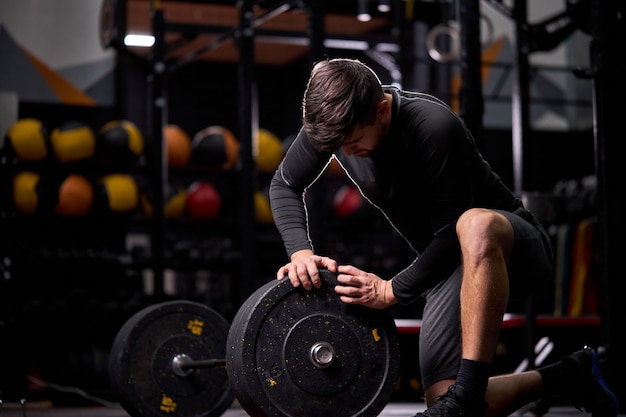 Esportista adicionando peso às placas pretas de mudança de barra, equipamento para o conceito de musculação. Jovem macho usando equipamentos esportivos para treinamento. na academia moderna sozinho