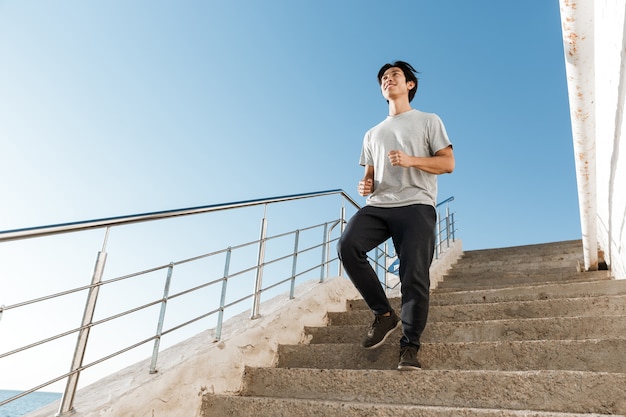 Esportista asiático saudável correndo ao ar livre, descendo as escadas