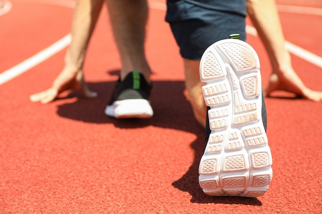 Esportista baixa começando a correr na pista atlética vermelha, close-up