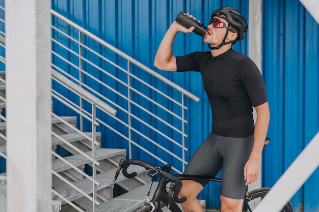 Esportista bebendo água sentado em uma bicicleta ao ar livre