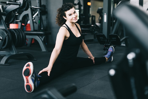 Esportista de fitness em roupas esportivas de moda fazendo corda e sentado no chão na academia. Vestuário e sapatos esportivos, estilo urbano.