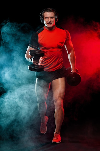 Esportista de fitness muscular homem atleta com halteres em ginásio de fitness Energia e potência Corredor e velocista em fones de ouvido