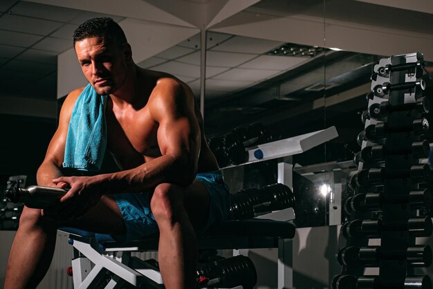 Esportista descansando após o treino. Homem na academia. Homem desportivo com torso nu. Cara de treino. Corpo atlético poderoso.