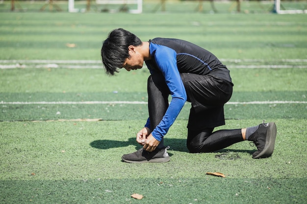 Esportista em roupas esportivas amarrando tênis. Jovem asiático parando de amarrar o sapato ao ar livre.