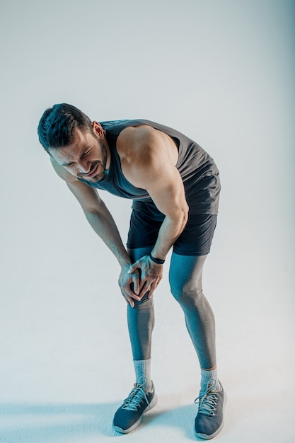 Esportista exausto, sentindo dores no joelho. jovem barbudo homem europeu usa uniforme esportivo. conceito de lesão desportiva. isolado em fundo turquesa. sessão de estúdio