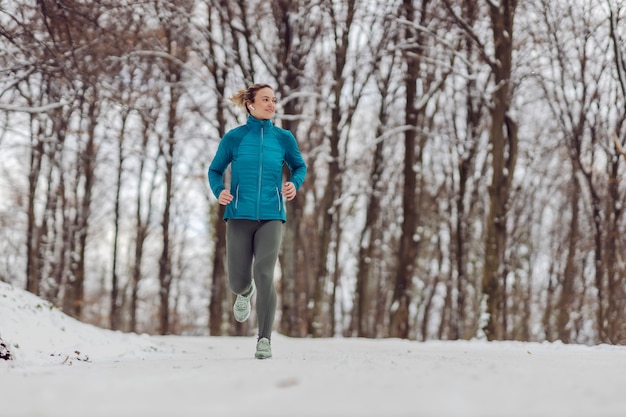 Esportista magro correndo na floresta em um clima de neve. clima frio, neve, vida saudável, boa forma, hábitos saudáveis, natureza
