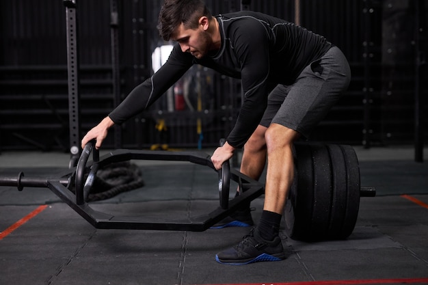 Esportista movendo pesos ou barra transversal na academia, troca de equipamento, suporte segurando barra, jovem macho vai para exercícios com equipamento esportivo, treinamento