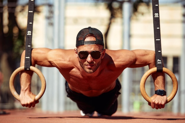 Foto esportista muscular exercitando-se em anéis de ginástica ao ar livre no ginásio ao ar livre mãos em anéis mergulhando homem fazendo exercício usando anéis