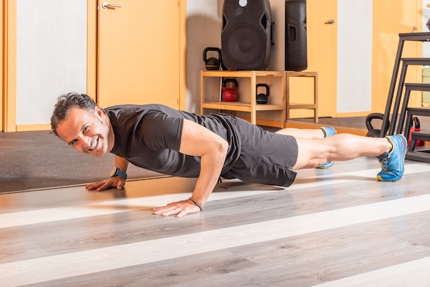 Esportista, olhando para a câmera com sorriso, fazendo flexões no clube de saúde. Conceito de exercícios no health club.