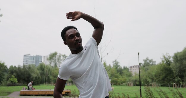 Esportista se preparando para um treino ao ar livre no parque. Homem afro-americano, esticando os braços ou aquecimento. Corrida saudável do conceito e exercício ao ar livre.