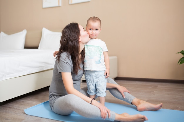 Esportiva linda mãe grávida com filho bebê, exercitando-se na esteira de ioga azul. maternidade atlética e saudável. fitness, maternidade feliz e conceito de estilo de vida saudável.