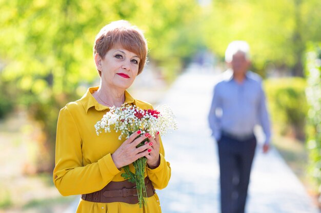 Una esposa anciana con flores espera en el parque a su marido.