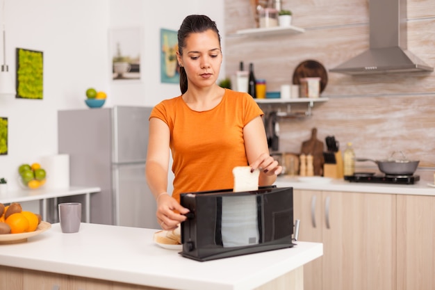 Esposa assando fatias de pão na torradeira elétrica para o café da manhã.